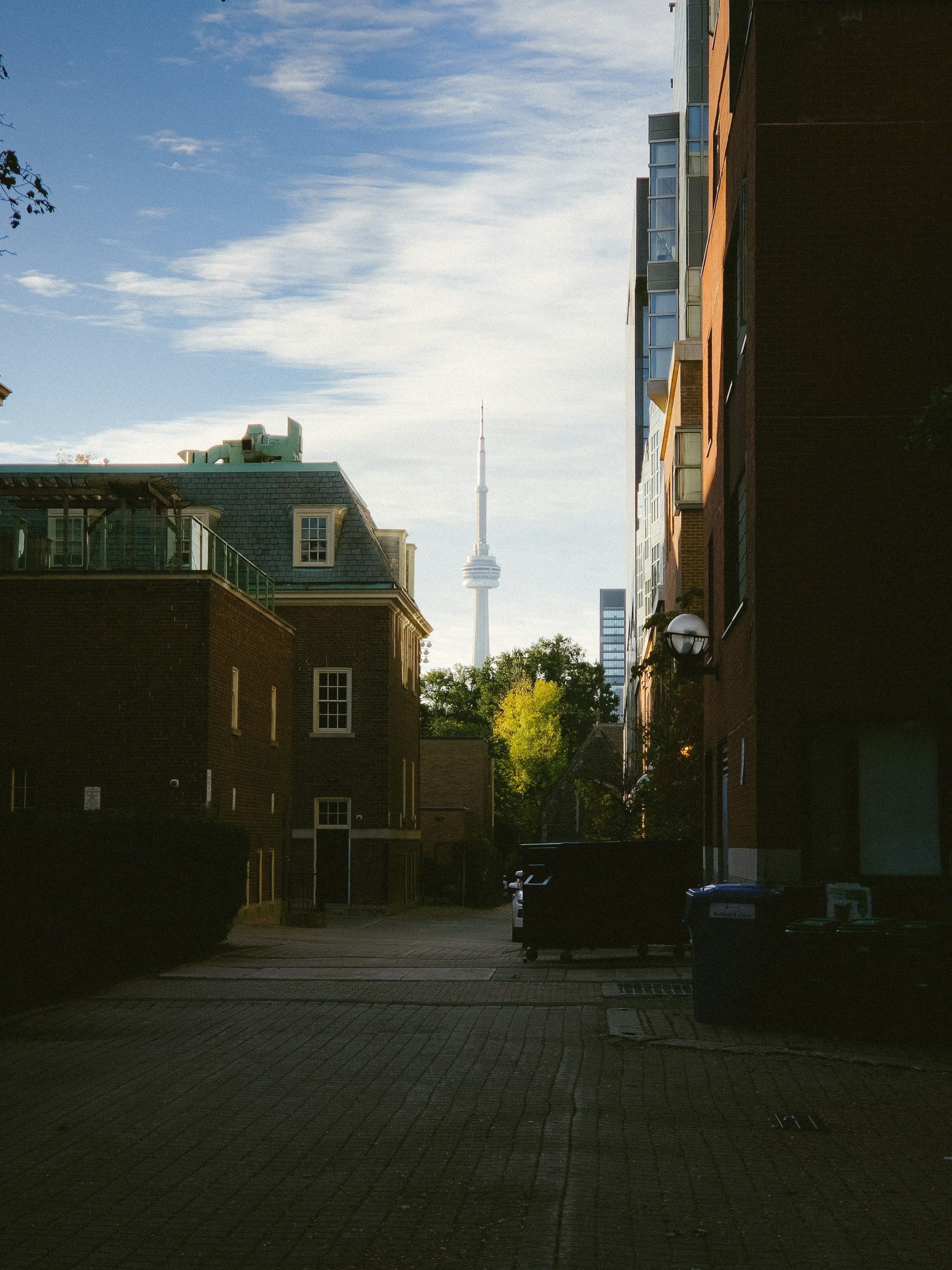 A campus alley at dusk with the CN Tower in the gap between the buildings.